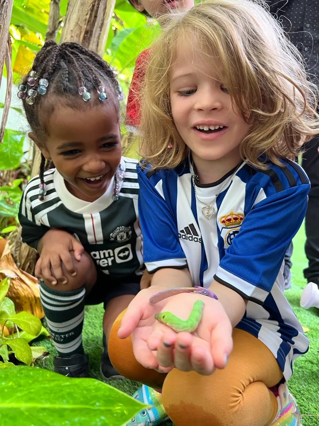 Two children crouching in the garden, delighted by a caterpillar held in one of their hands