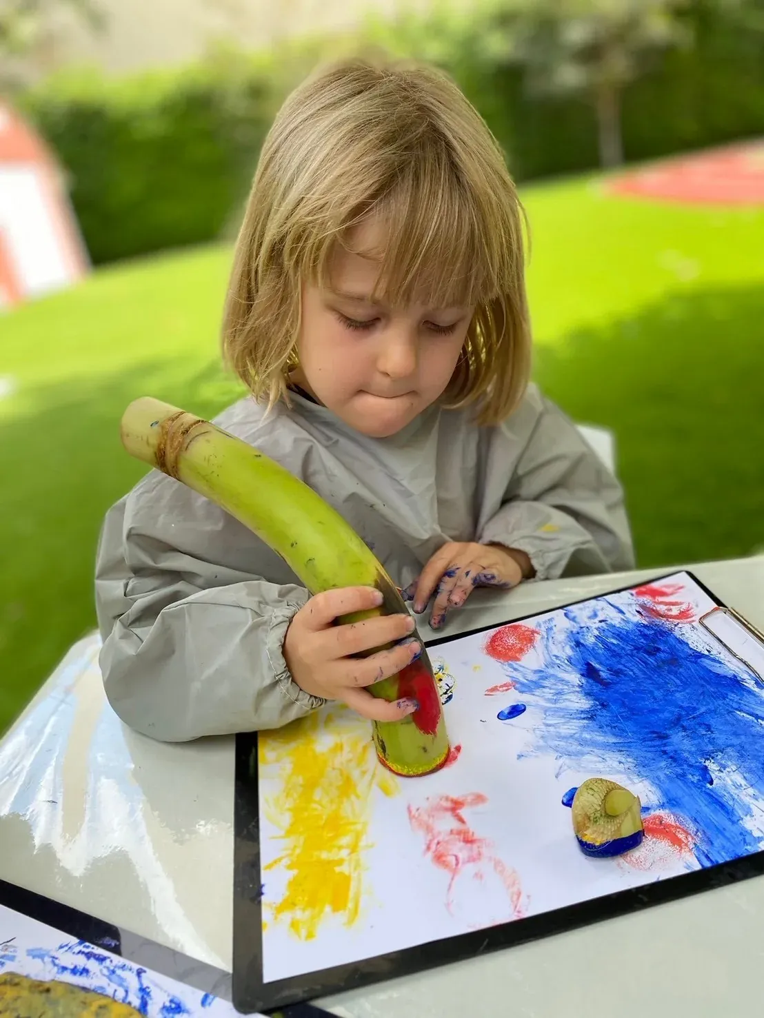 A girl printing with the cut end of a banana stem in red, yellow and blue