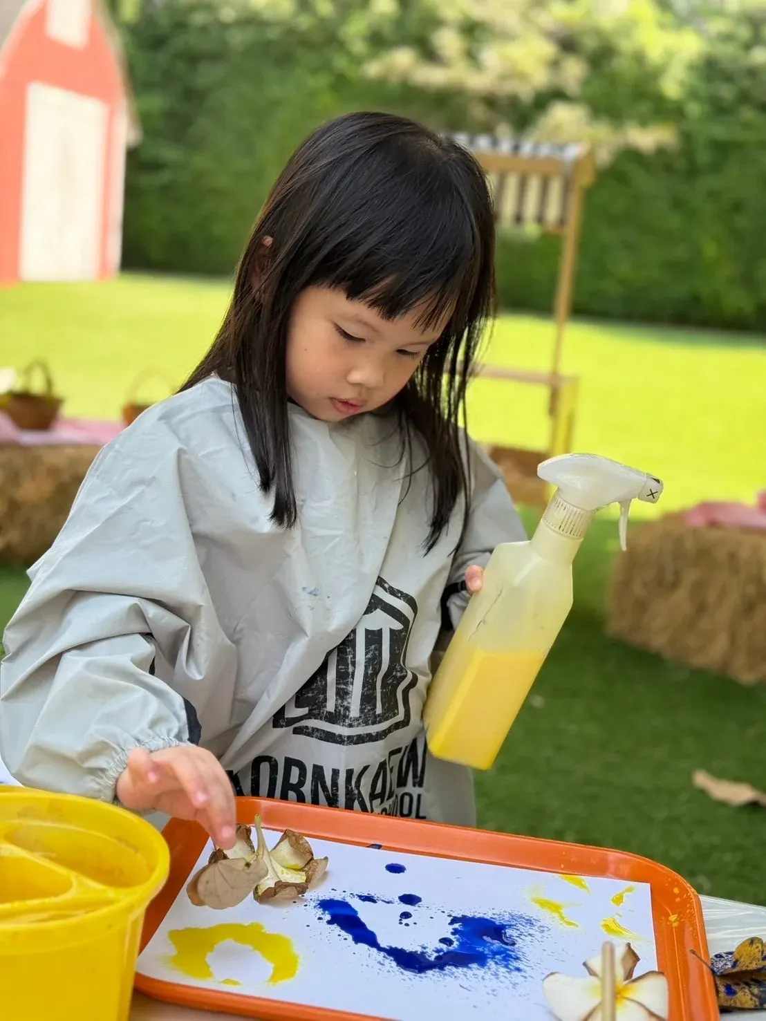A girl spraying yellow paint around leaves and flowers laid on her paper