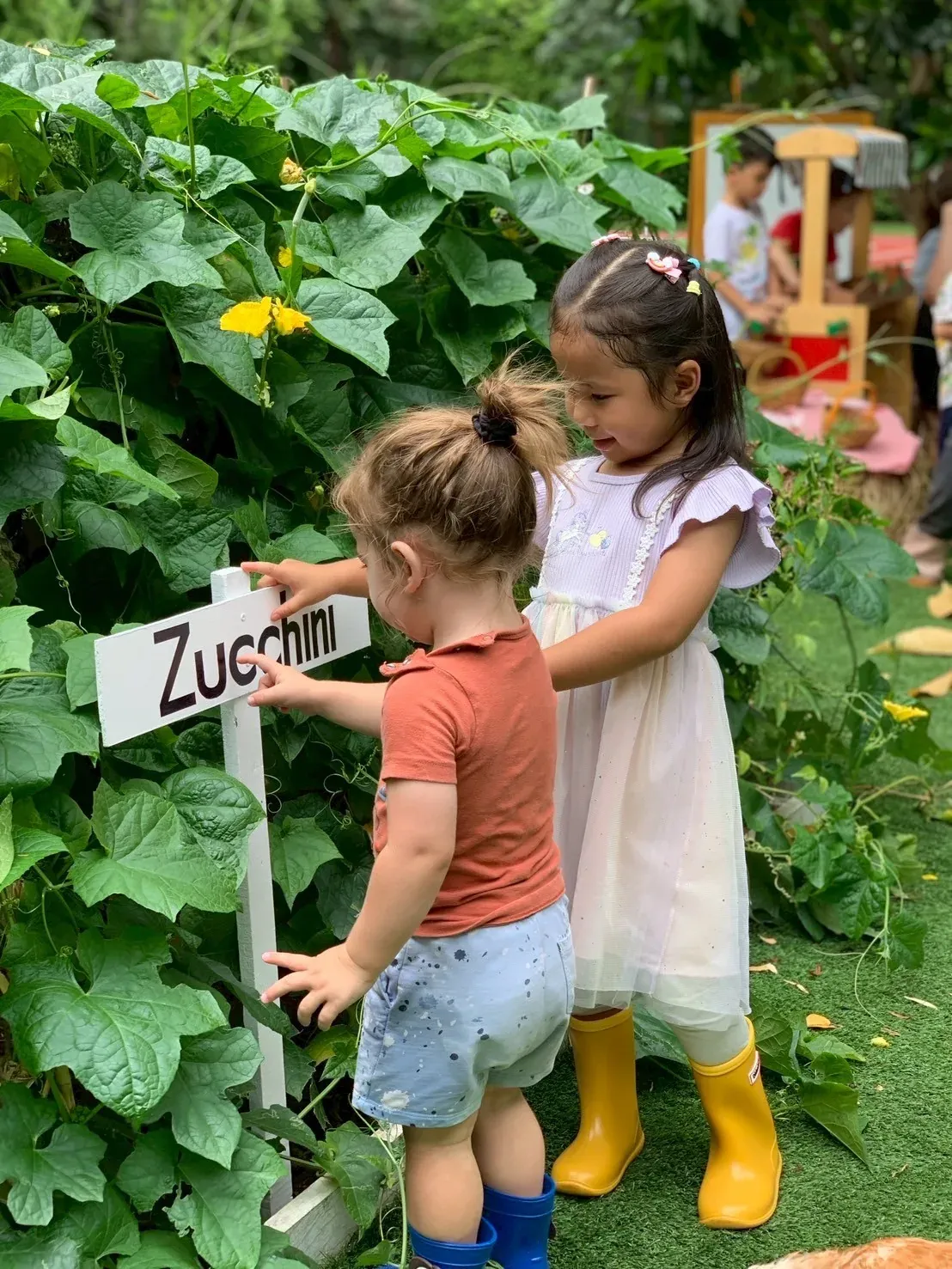 Two girls in wellies reading the zucchini sign in the vegetable garden