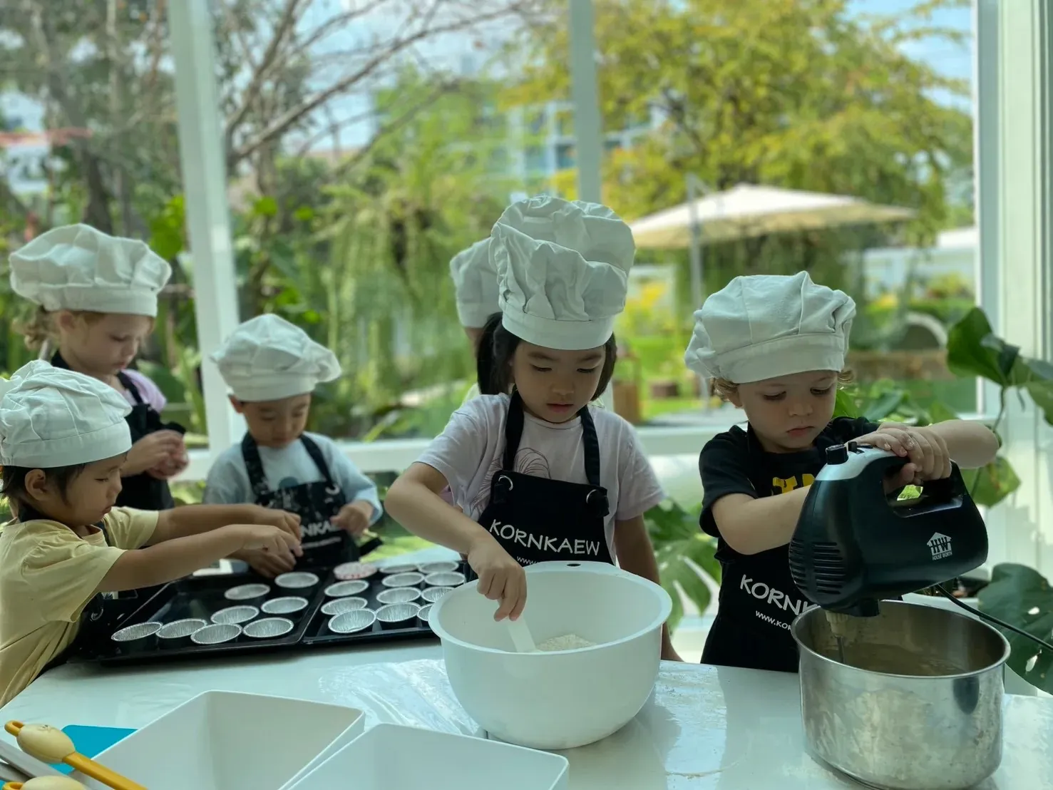 Children in chef hats sifting flour, mixing batter and lining the muffin trays