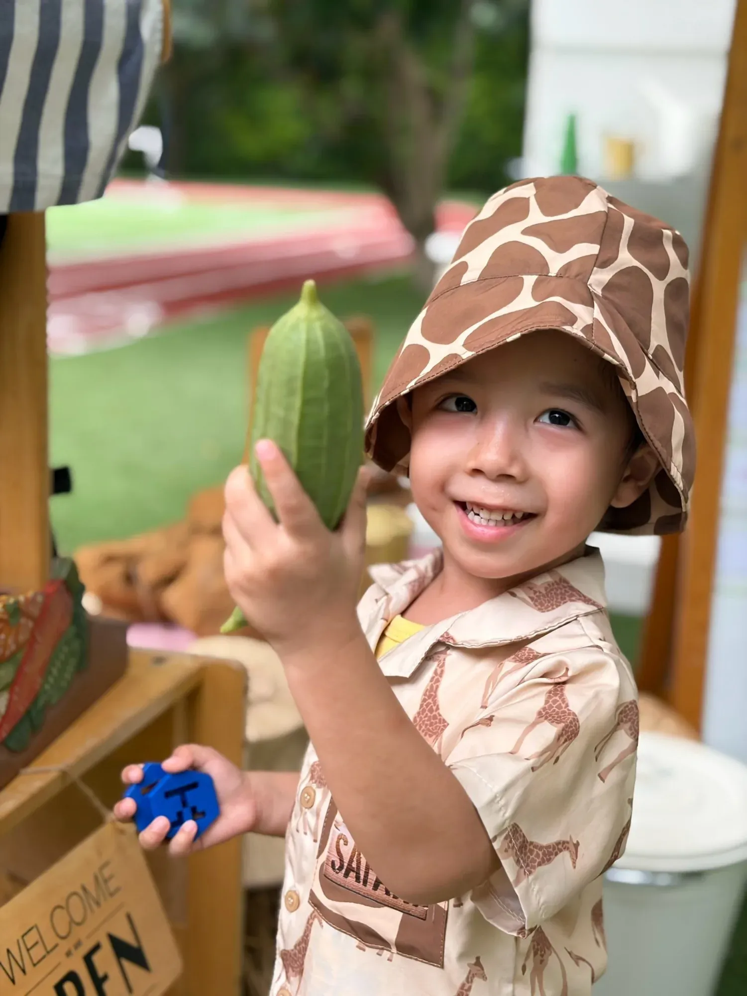 A boy in a giraffe hat choosing a vegetable, a KIMS coin in his other hand
