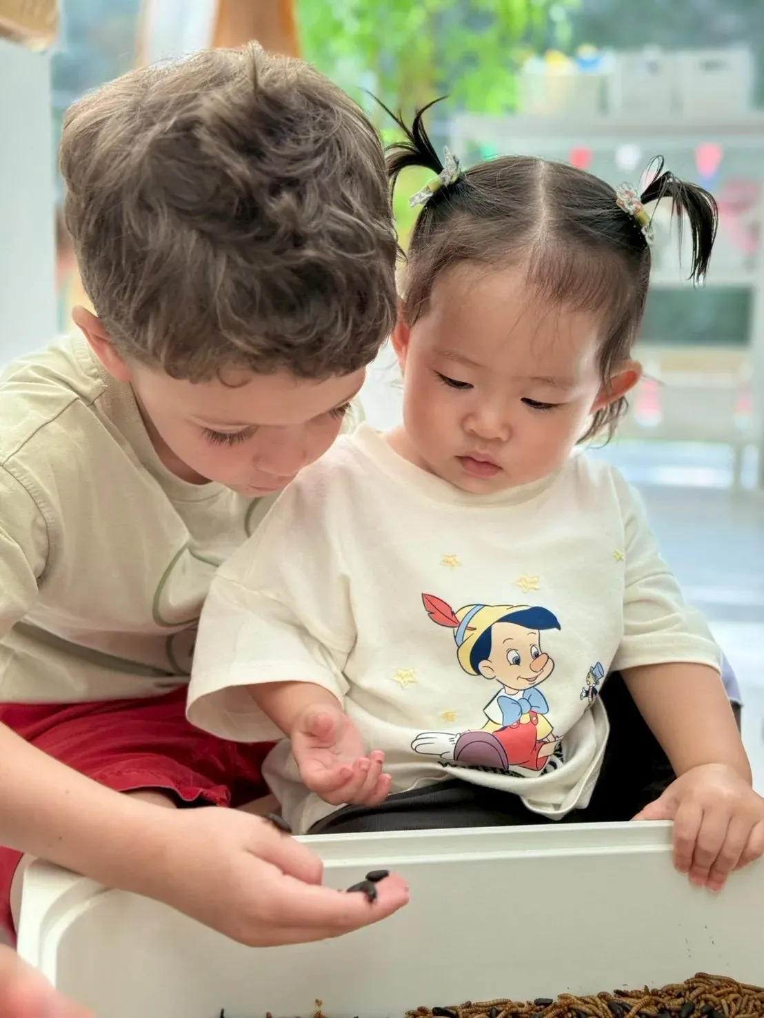 Two children looking closely at a beetle held in a boy’s hand, over the mealworm tray