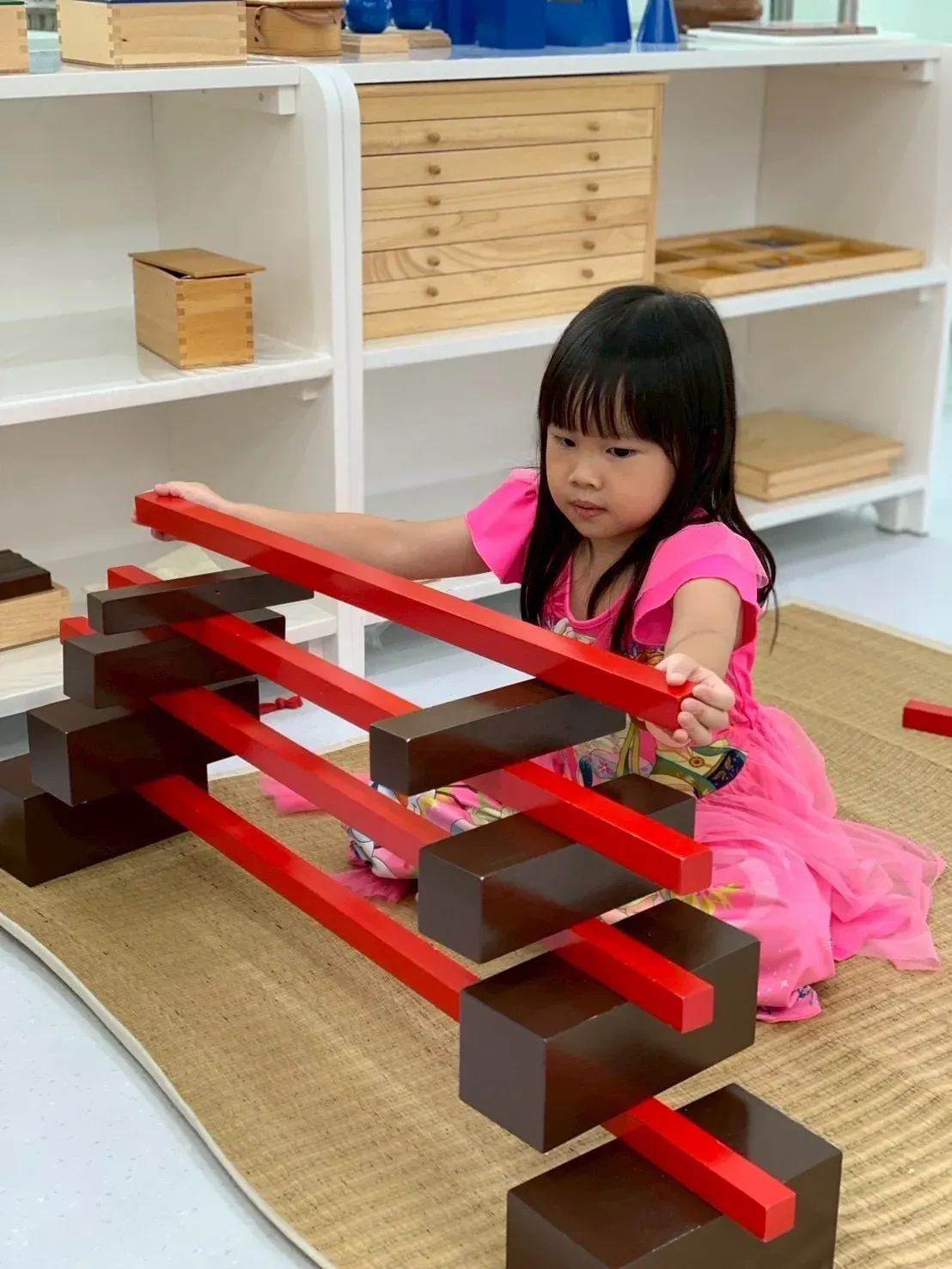 Sensorial: a girl building with the red rods and the brown stair