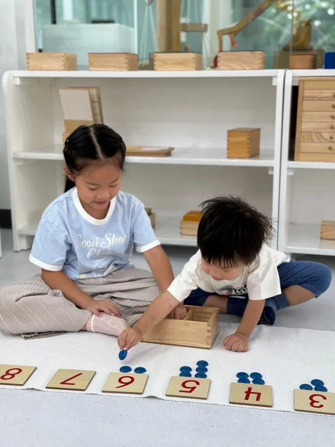 Mathematics: an older girl and a toddler placing counters under number cards