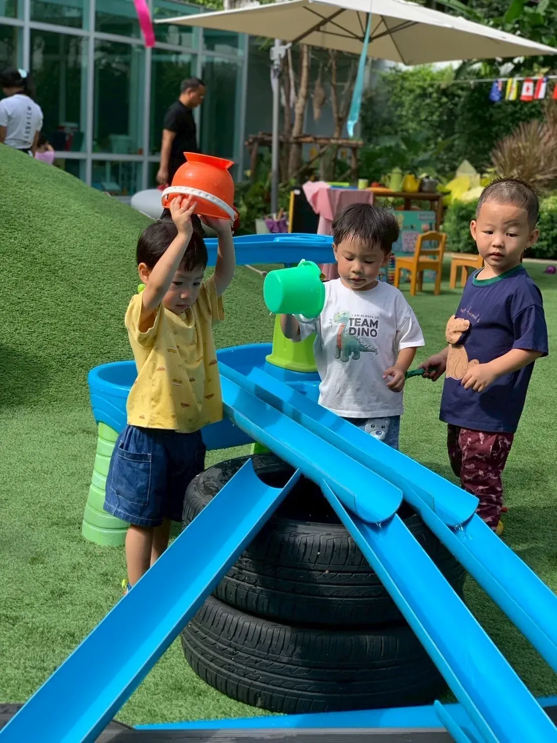Three toddlers pouring water down blue chutes at the water table