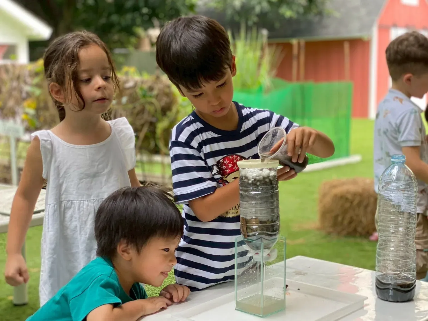 A boy pouring muddy water into the bottle filter the class built, friends watching