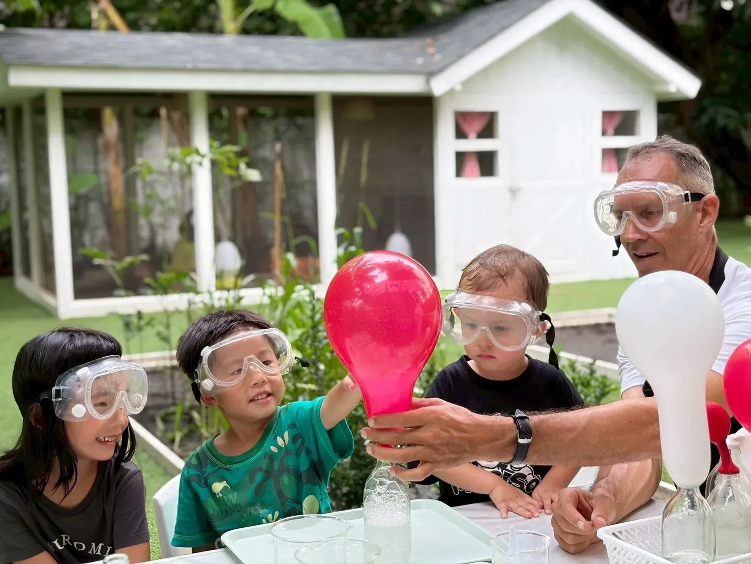 Children in goggles watching a balloon fill with gas from the bottle below