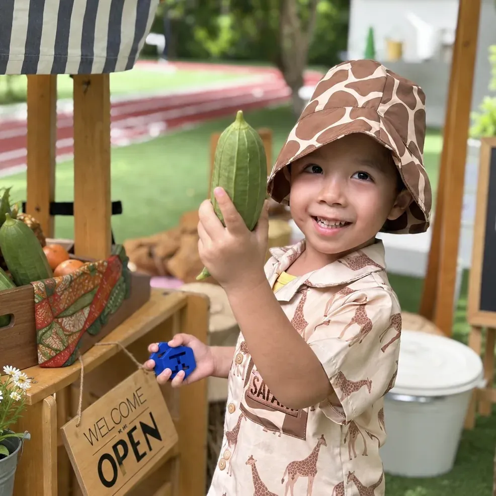 A smiling child holding up a vegetable at the market stall
