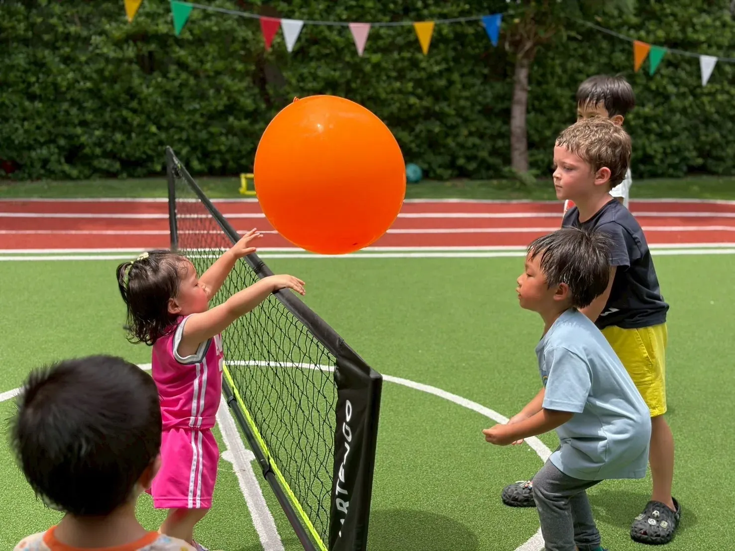 Children playing balloon volleyball over a low net on the sports field