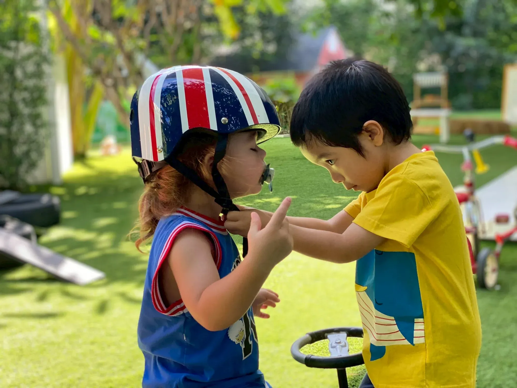 A boy fastening the helmet strap for a younger friend