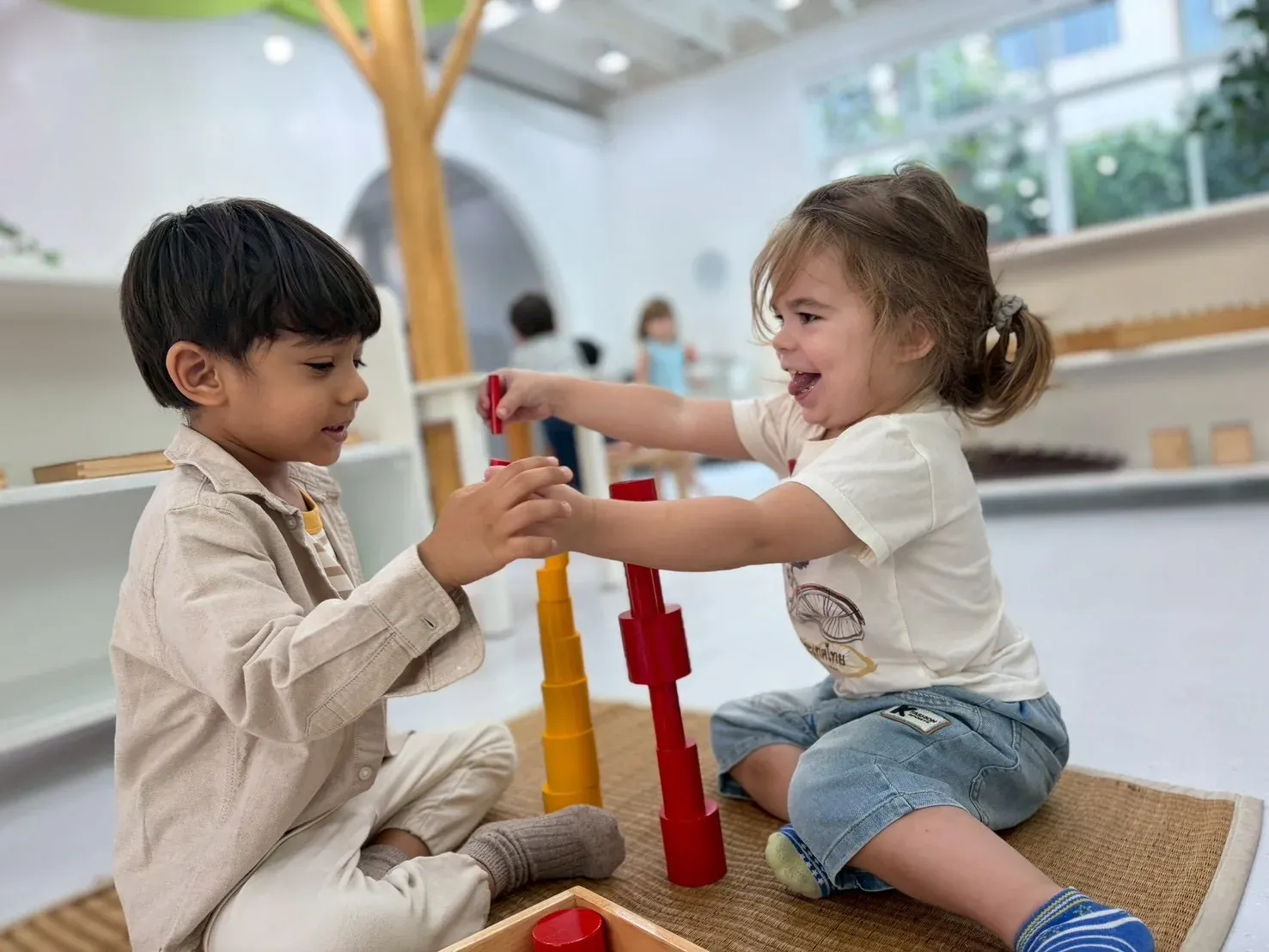 Two children building a tower together from Montessori cylinders